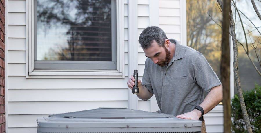 HVAC technician inspecting an outdoor air conditioner unit at a home